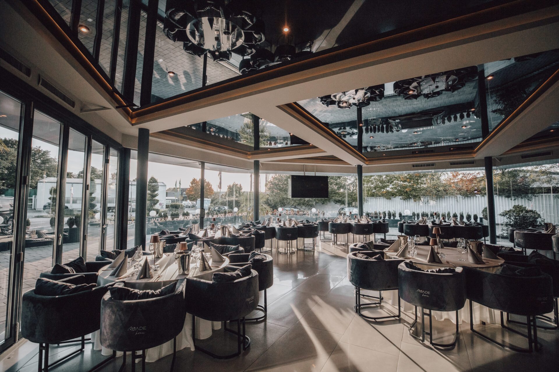 Großzügiger Blick auf den JADE Saal mit offener Fensterfront, runden Tischen und moderner Deckenbeleuchtung.
